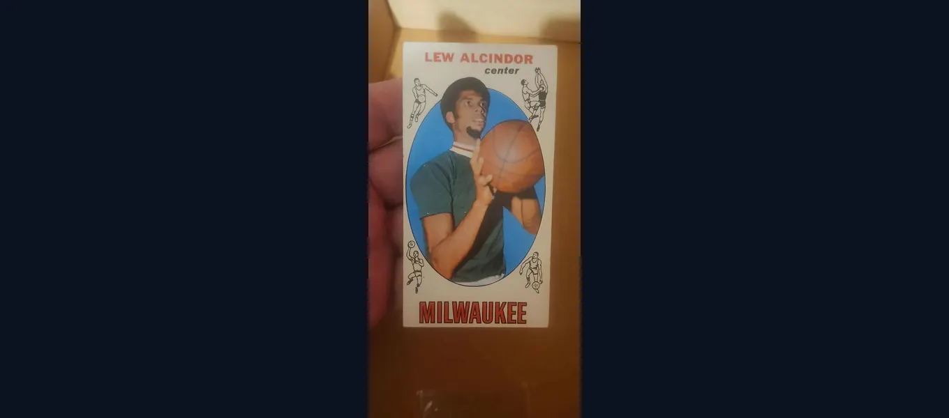 A raw, ungraded 1969-70 Topps Lew Alcindor rookie card held in hand, showing the tall-boy format and the Milwaukee nameplate