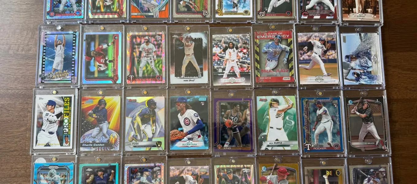 Rows of raw modern baseball rookie and prospect cards in toploaders, including refractors and coloured parallels, laid out on a wood table