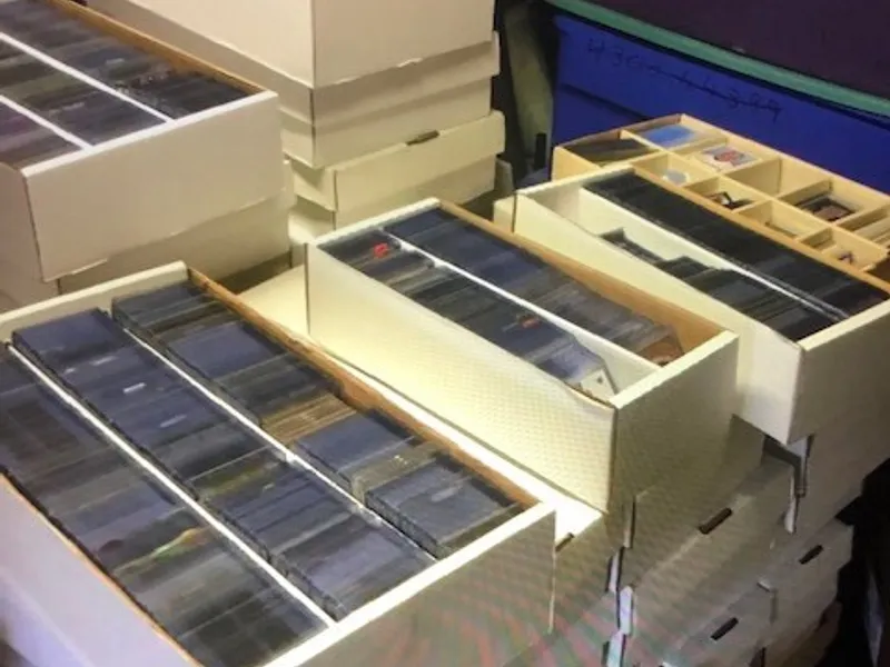 Stacked boxes of a purchased sports card collection, with rows of cards in penny sleeves and toploaders beside a sorting tray